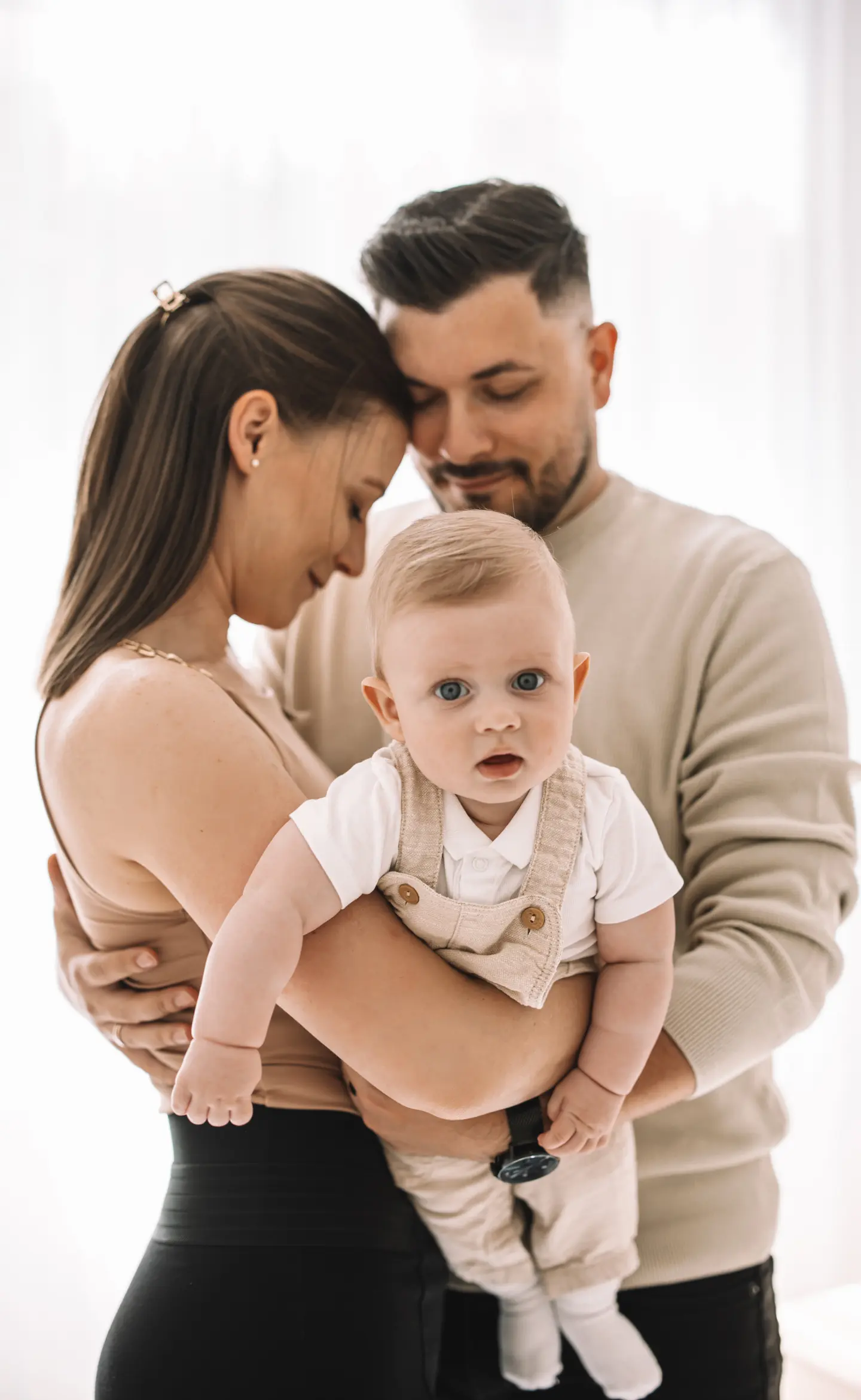 Családi portré egy kisbabával, szülők szeretettel ölelik körbe