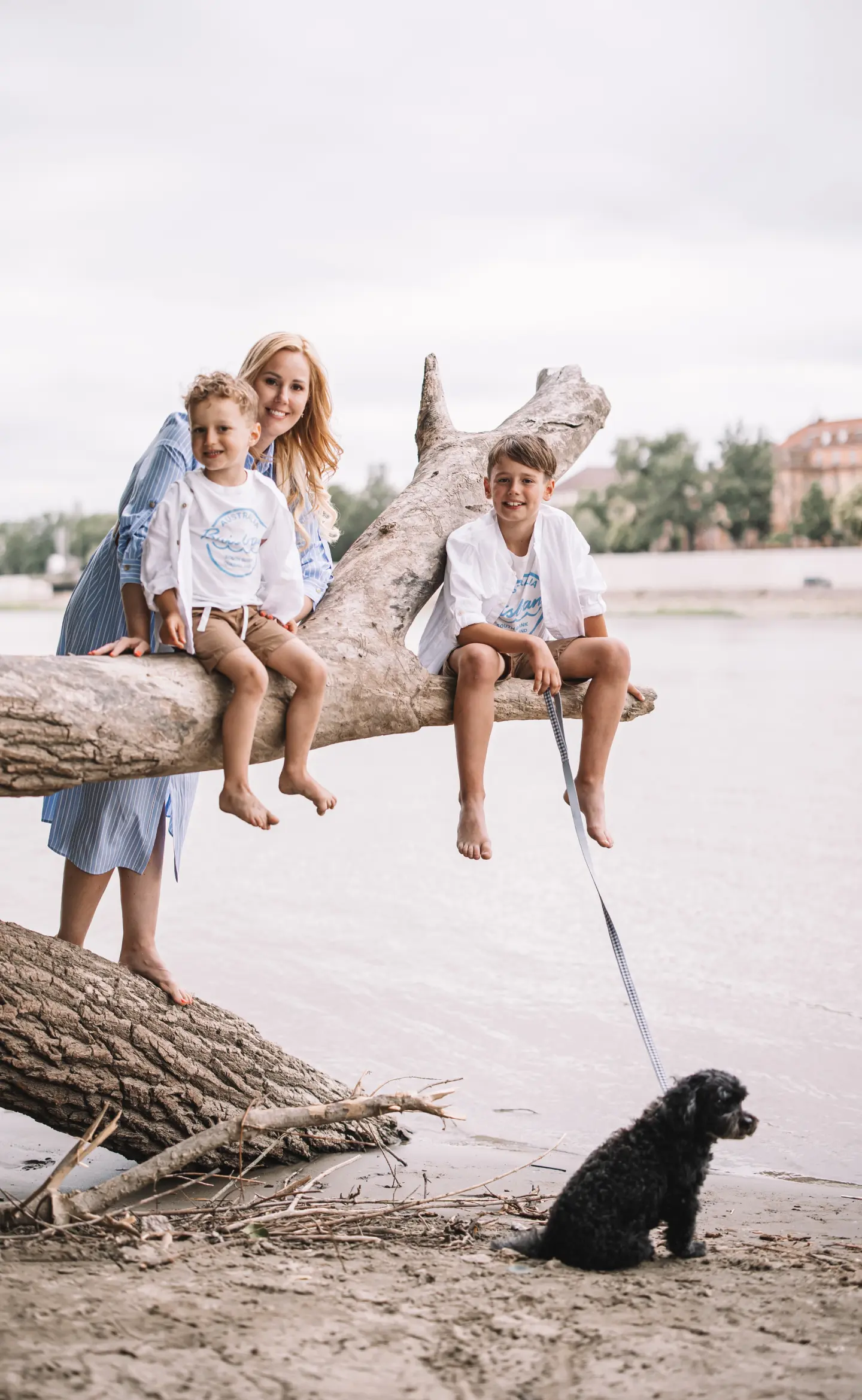 Anyuka két kisfiával egy fatörzsön ül, mellettük kis fekete kutya