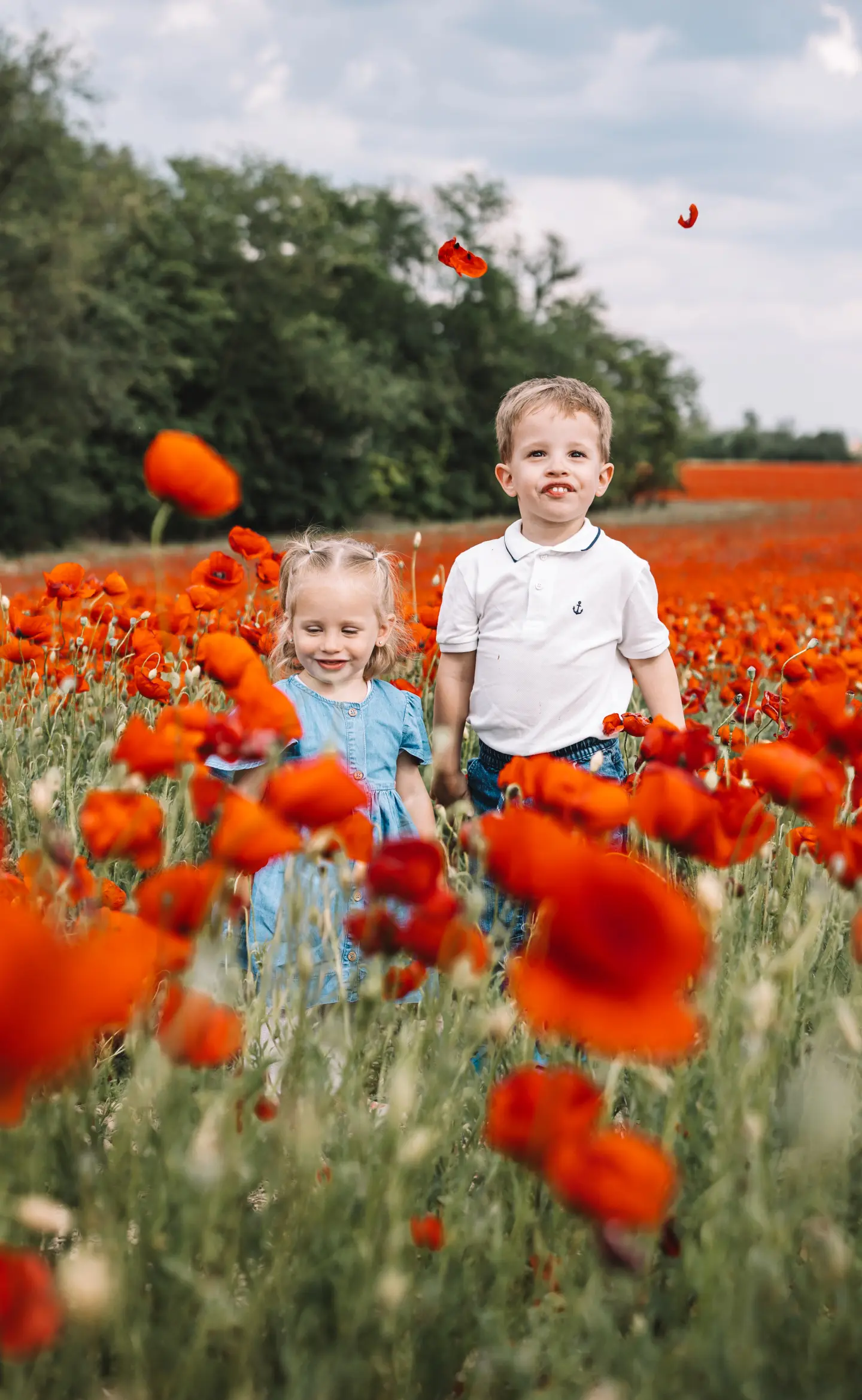 Két kisgyerek piros pipacsmezőben állva mosolyog a nyári fényben