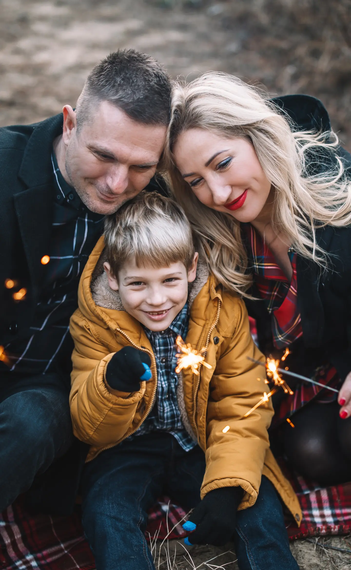 Kisfiú sárga kabátban csillagszóróval, szülei ölelésében piknik pokrócon