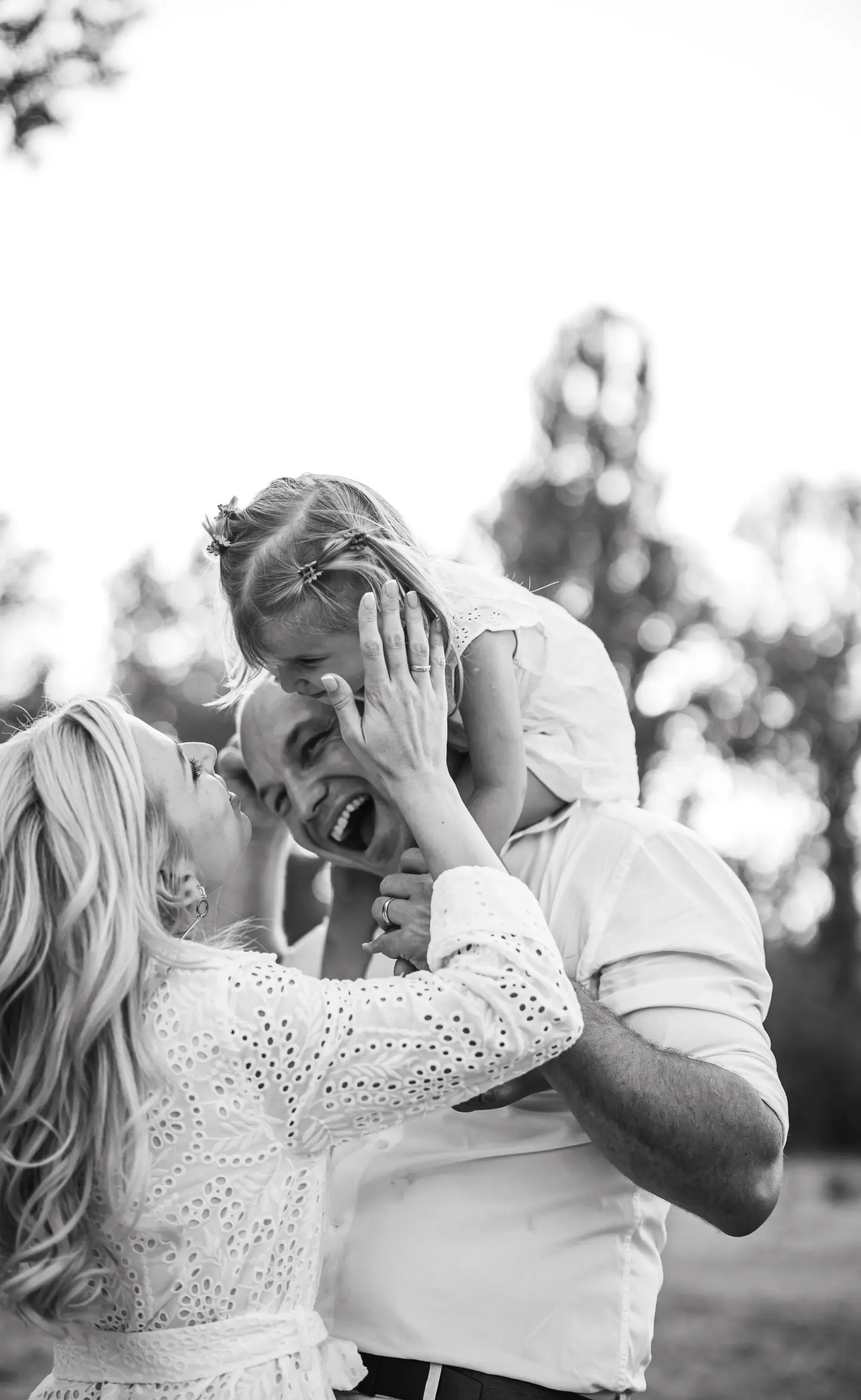 Nevető család ölelkezik egy szabadtéri fotózáson, kislány apukája nyakában ül