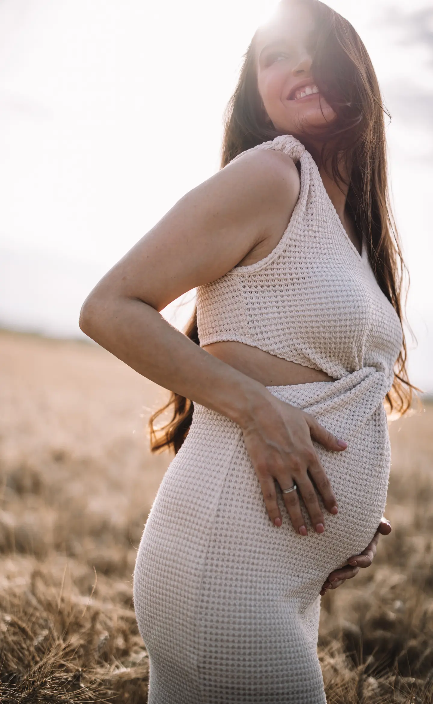 Mosolygó kismama napfényes mezőn, természetes kismamafotózáson