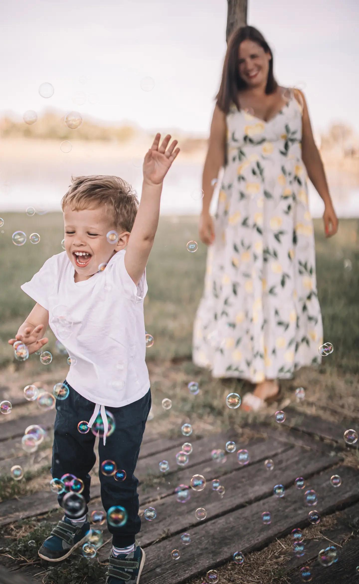 Kisfiú buborékokat kerget, háttérben édesanyjával egy nyári szabadtéri fotózáson