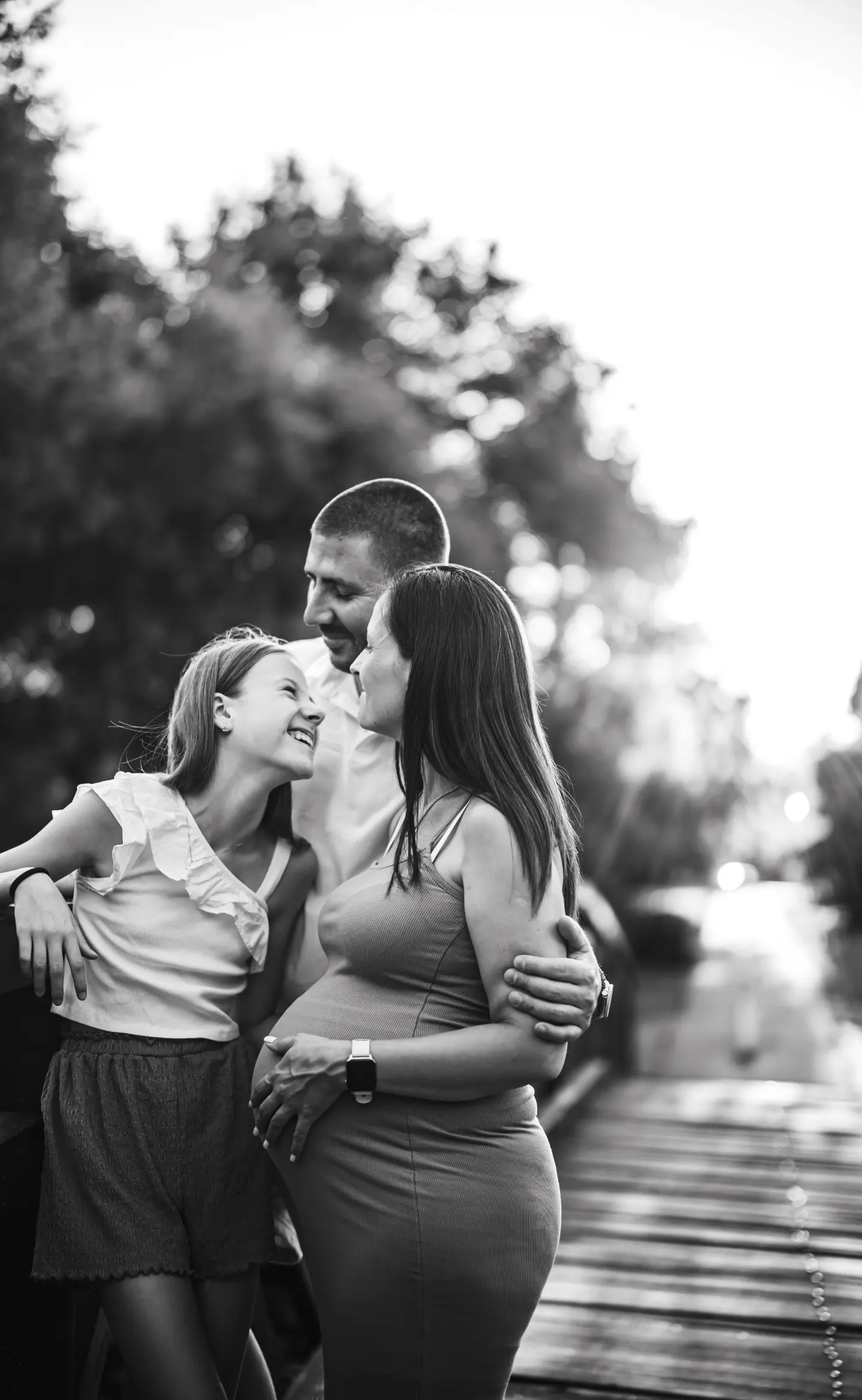 Várandós nő családjával mosolyogva egy hídon, fekete-fehérben