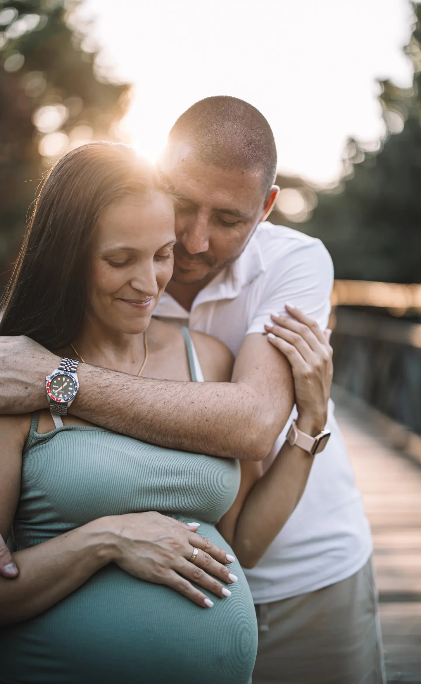 Kismama és párja meghitt ölelésben, naplementés háttérrel