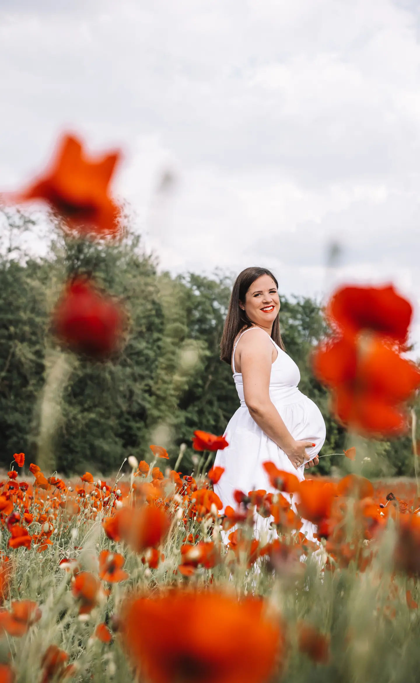 Kismama fehér ruhában pipacsmezőn, természetes fényben