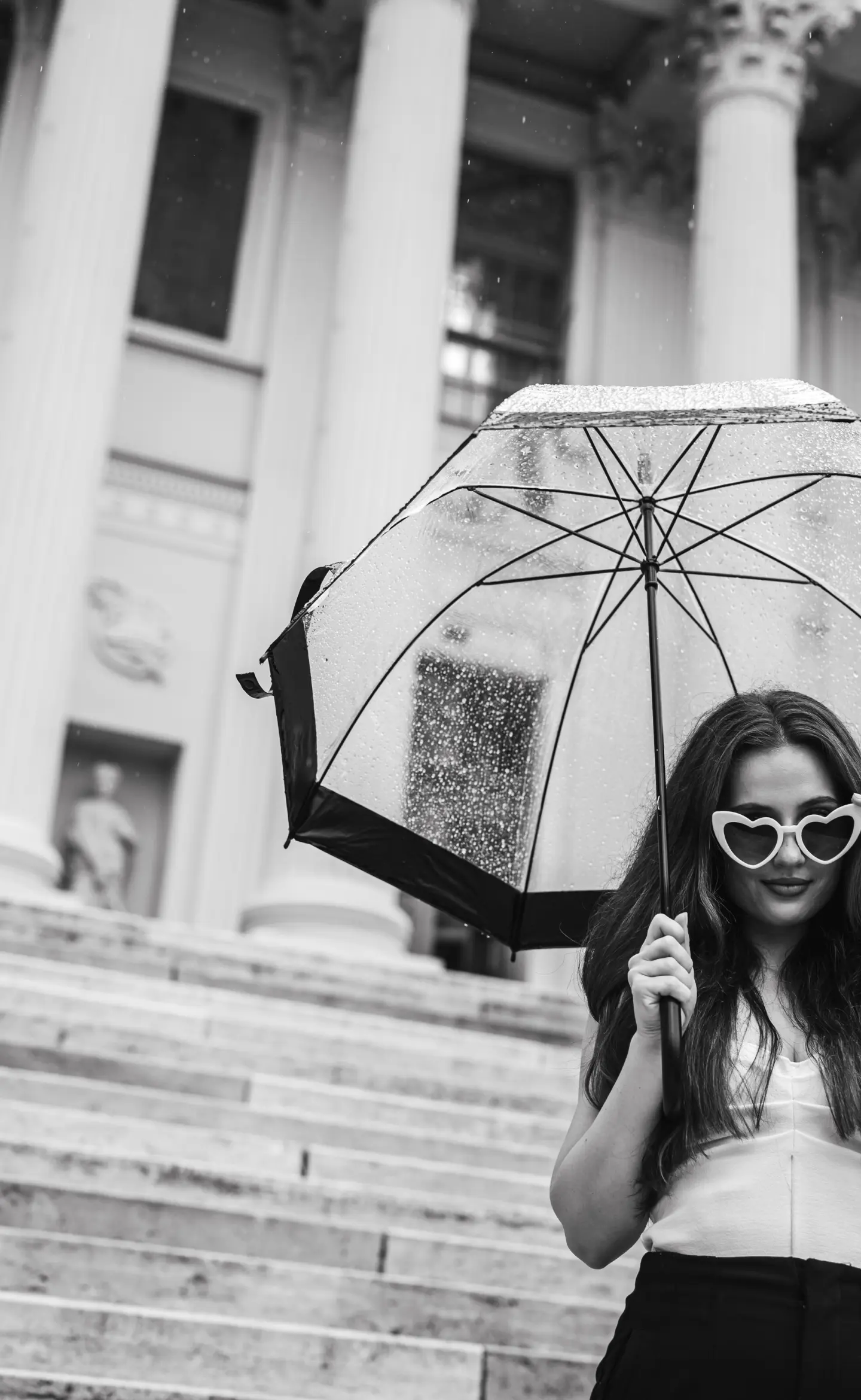 Egy nő esernyővel áll egy oszlopos épület lépcsőjén, miközben esik az eső., portré fotózás