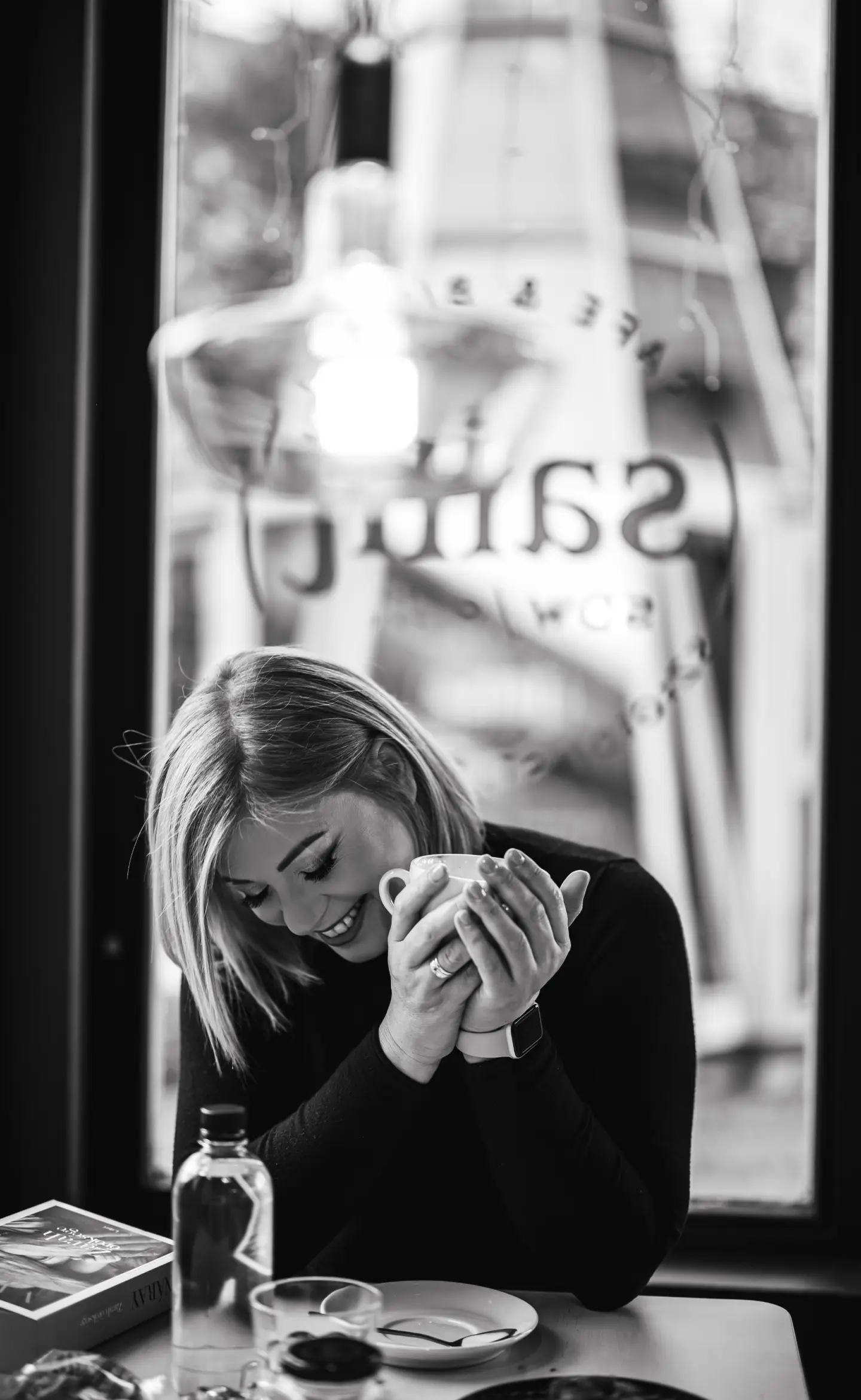 egy nő a bögréjét szorongatva nevet egy kávézóban, az asztal felé néz, portré fotózás