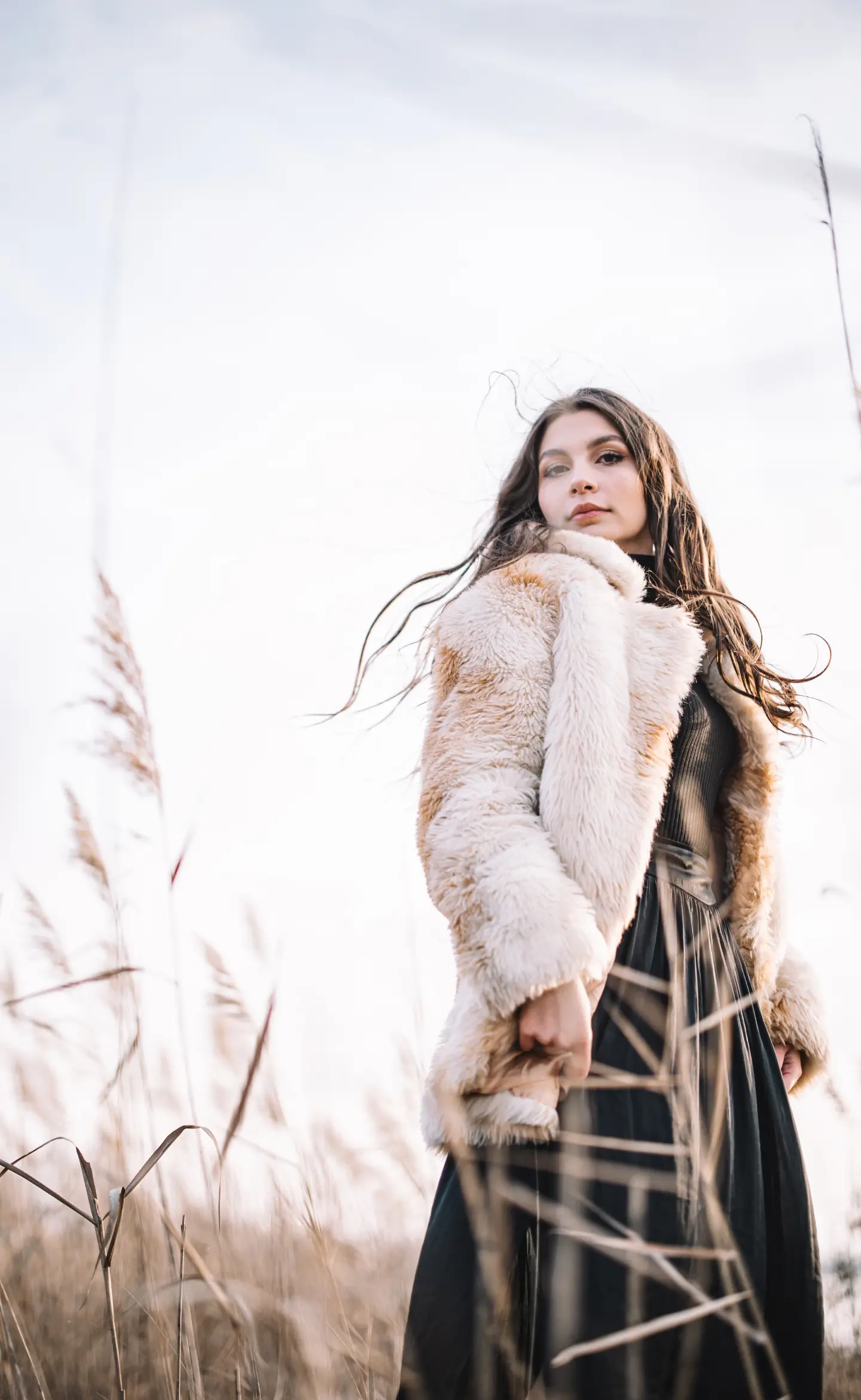 egy hosszú barnahajú lány szörmebundában áll a nádasban, éppen a kamerába néz, portré fotózás
