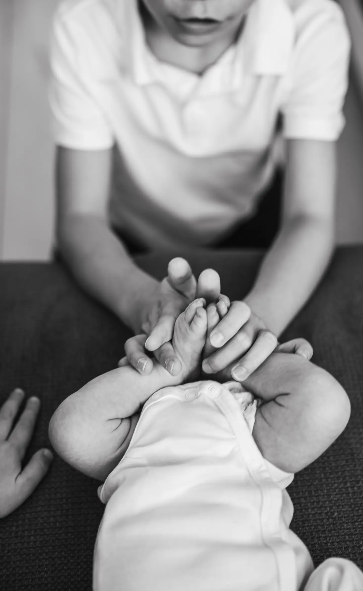 Nagyobb testvér gyengéden fogja újszülött testvére lábait fekete-fehér fotón