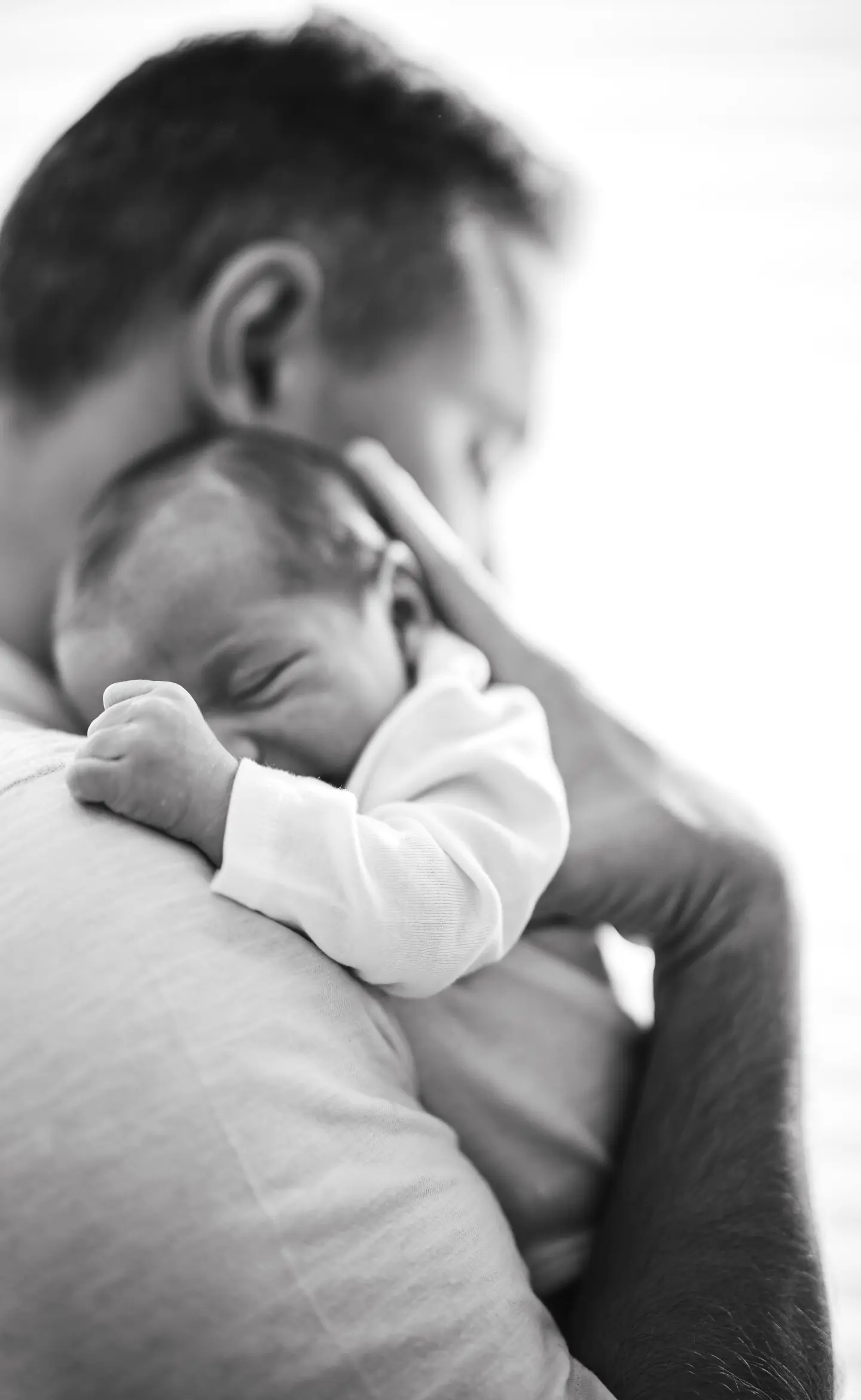Fekete-fehér fotó egy apuka vállán pihenő újszülött babáról