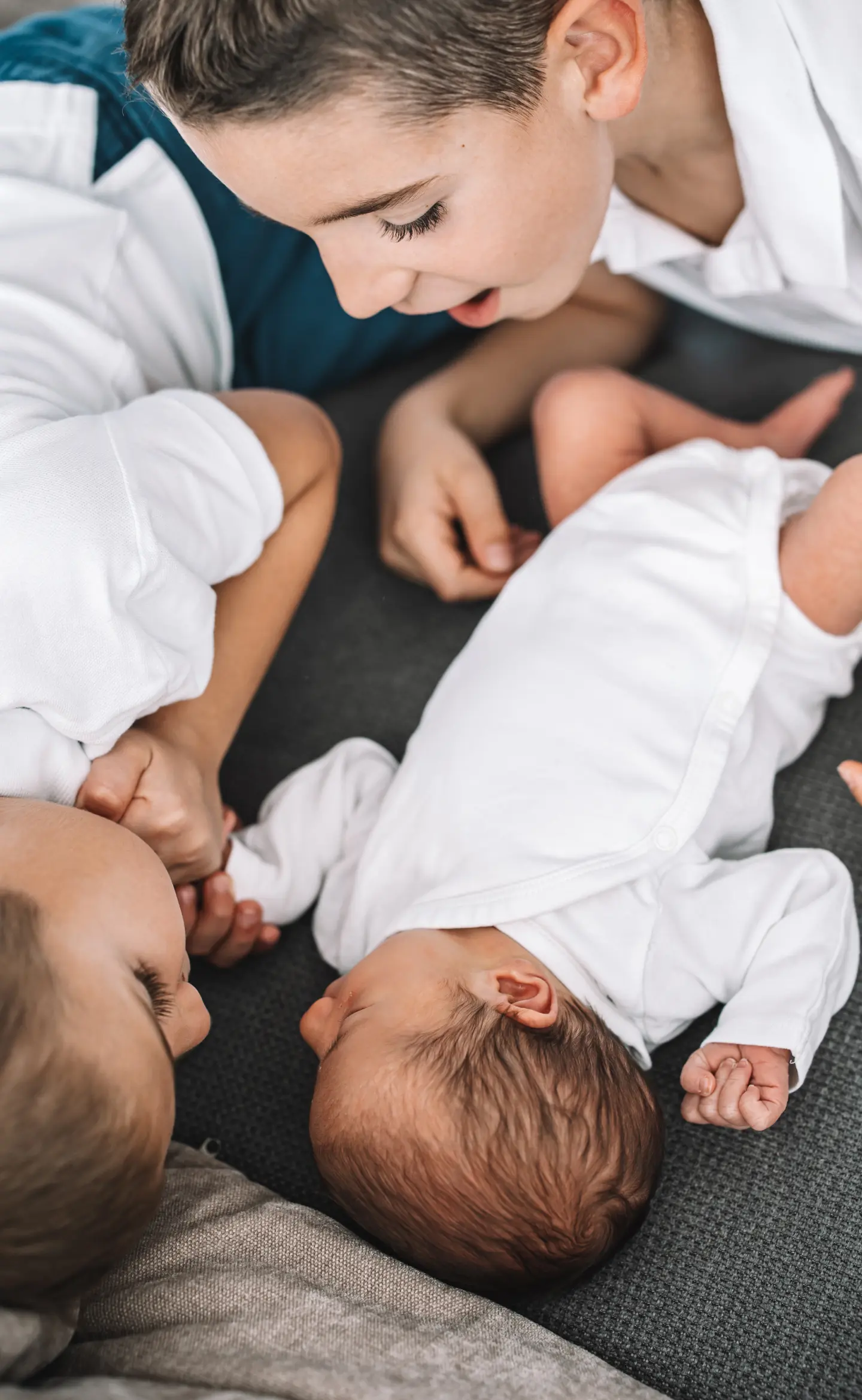 Két nagyobb testvér nézi és simogatja újszülött kisöccsüket a kanapén