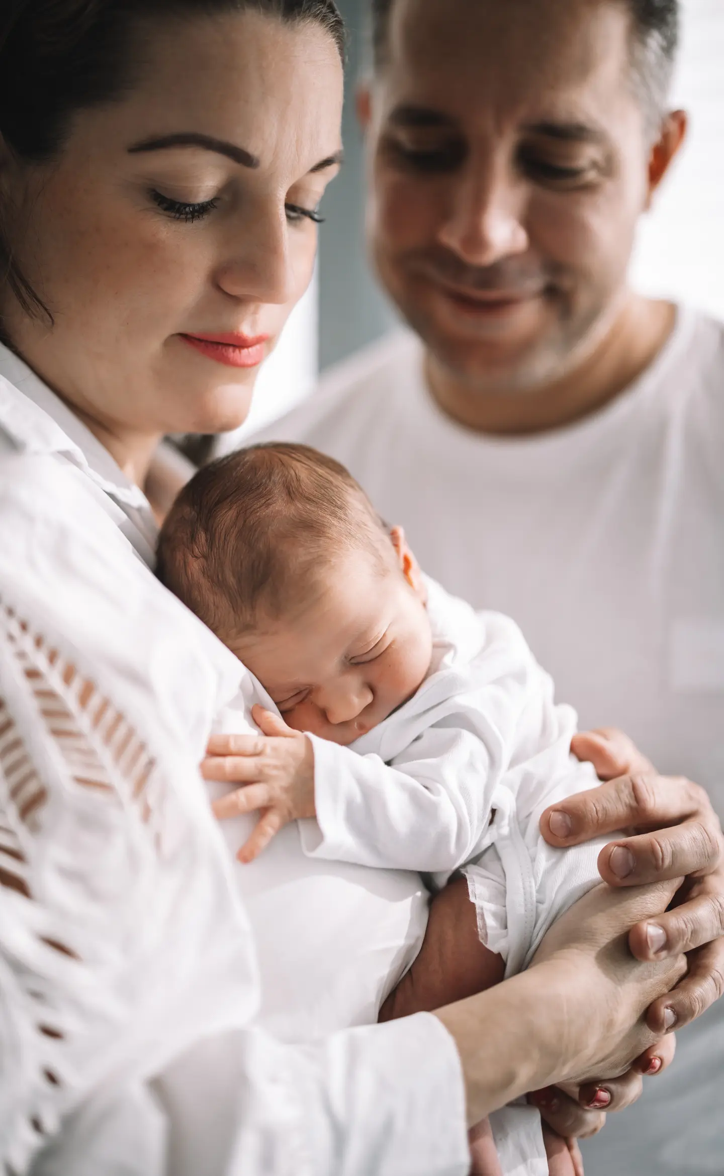 Újszülött baba alszik az édesanyja karjában, miközben az apuka szeretettel nézi őket