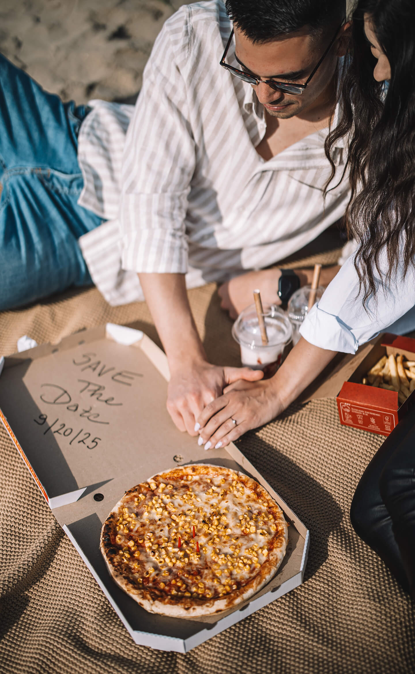 Jegyespár pizzás dobozra írva jelzi esküvőjük dátumát egy piknik során