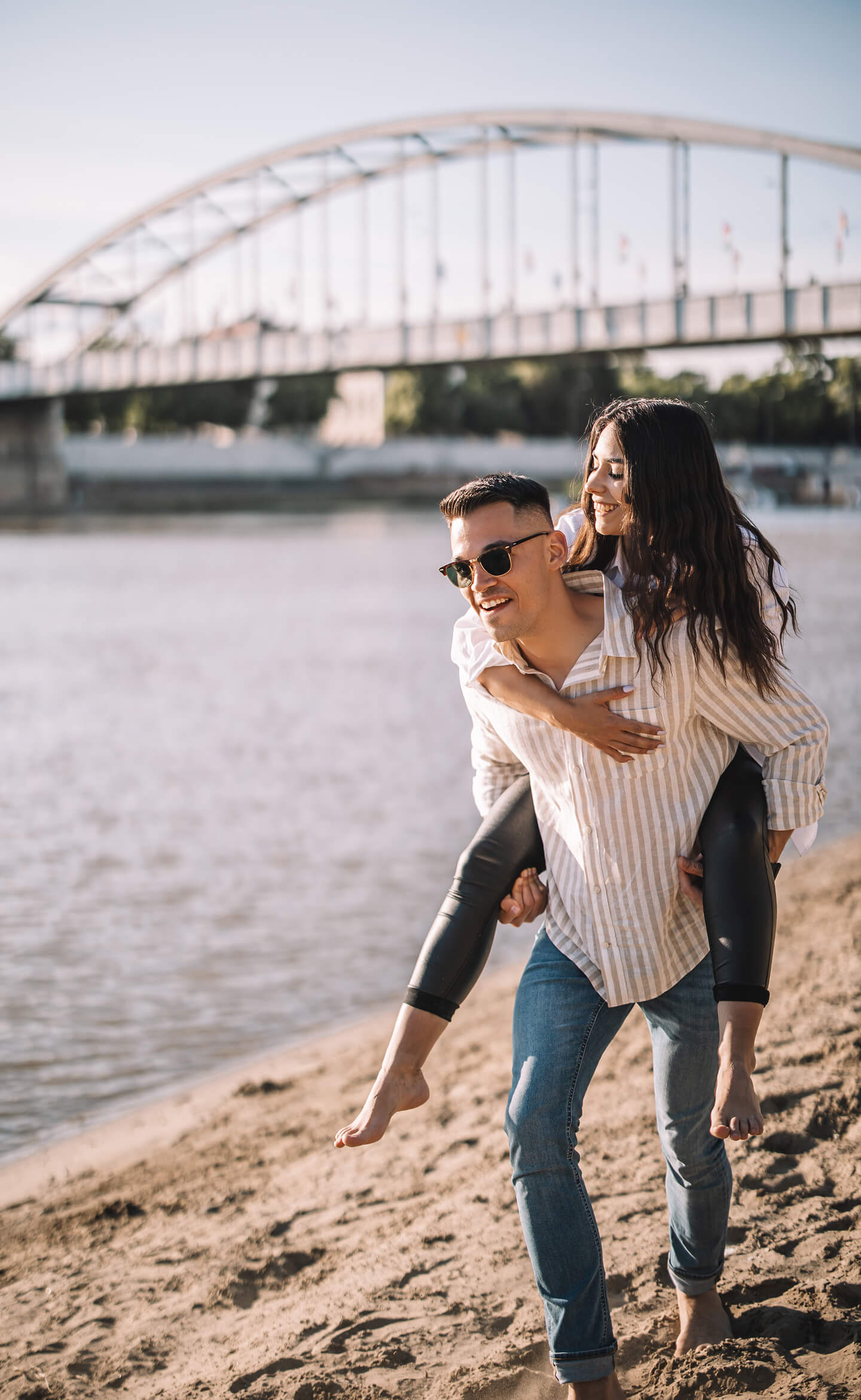 Fiú a vízparton cipeli a barátnőjét játékosan a hátán