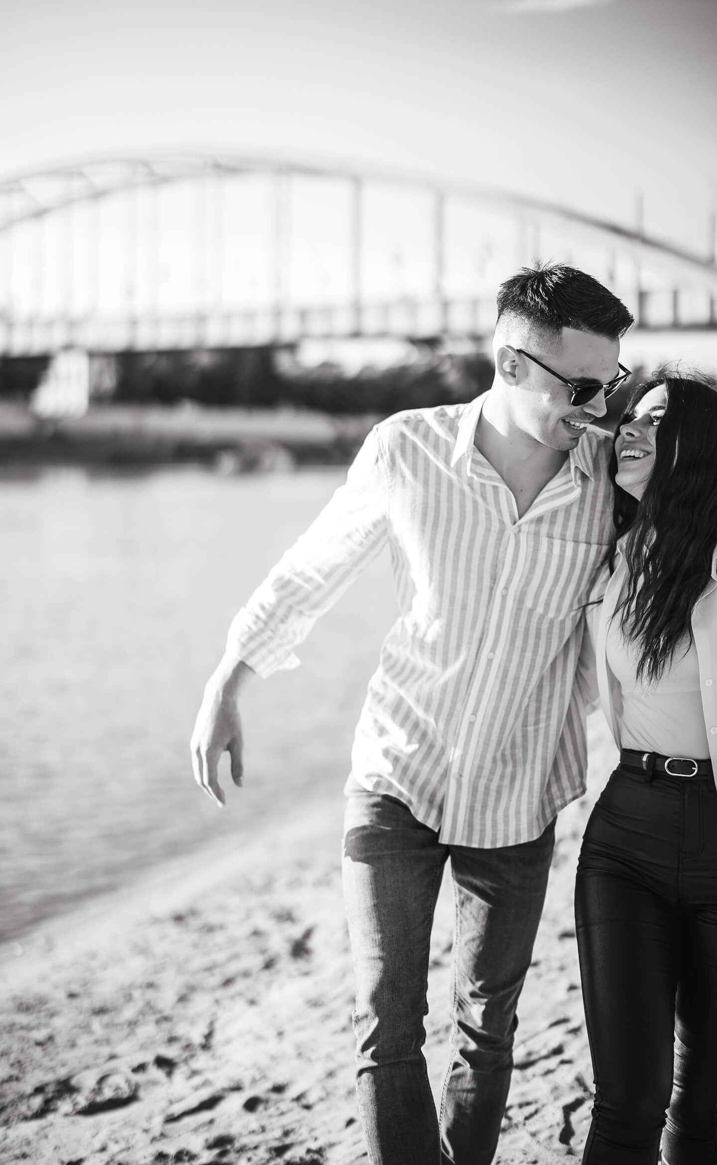 Szerelmes pár kézen fogva sétál a vízparton, fekete-fehér portré