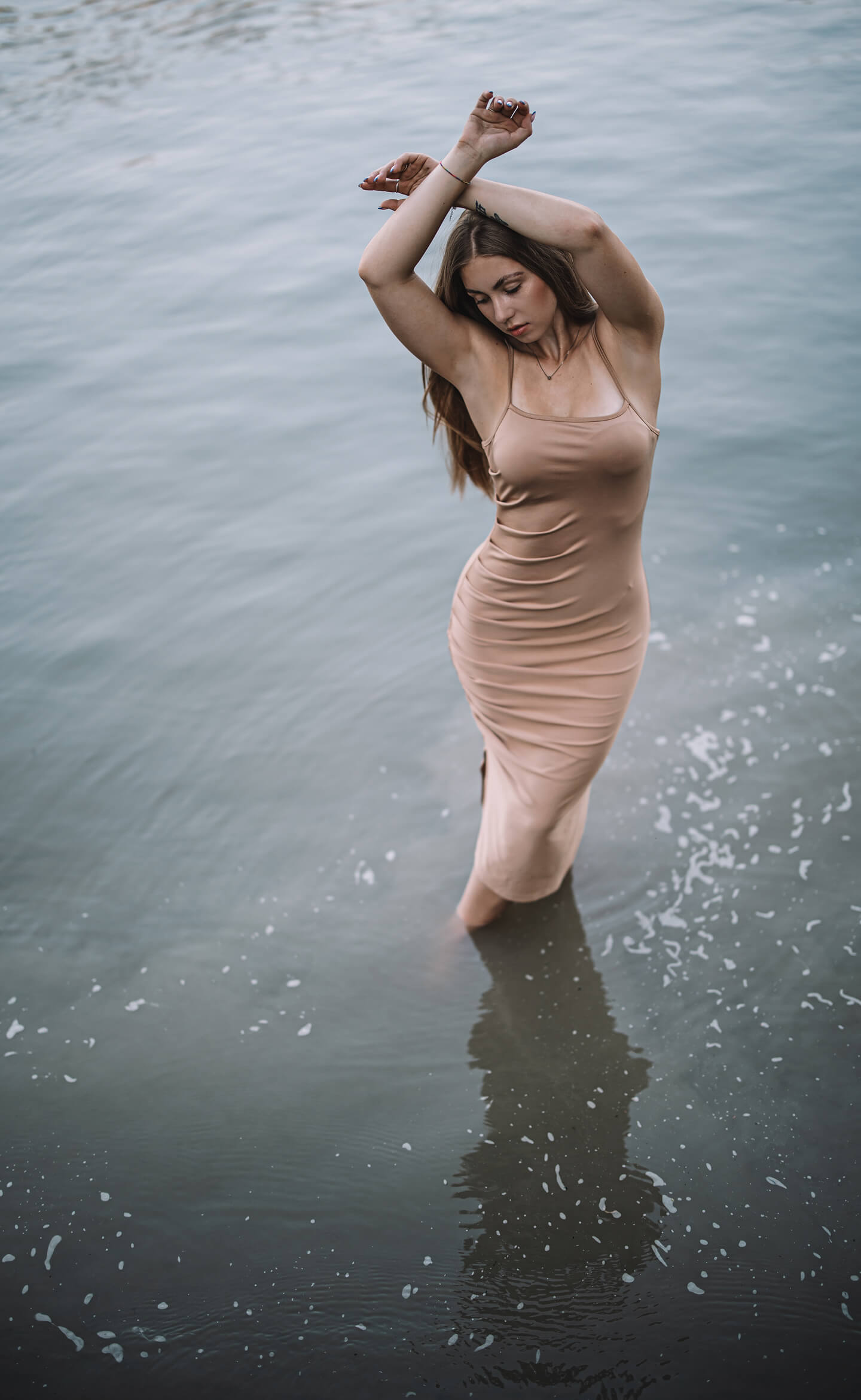 Fiatal nő testhez simuló ruhában áll a vízben, kezeit a feje fölé emelve