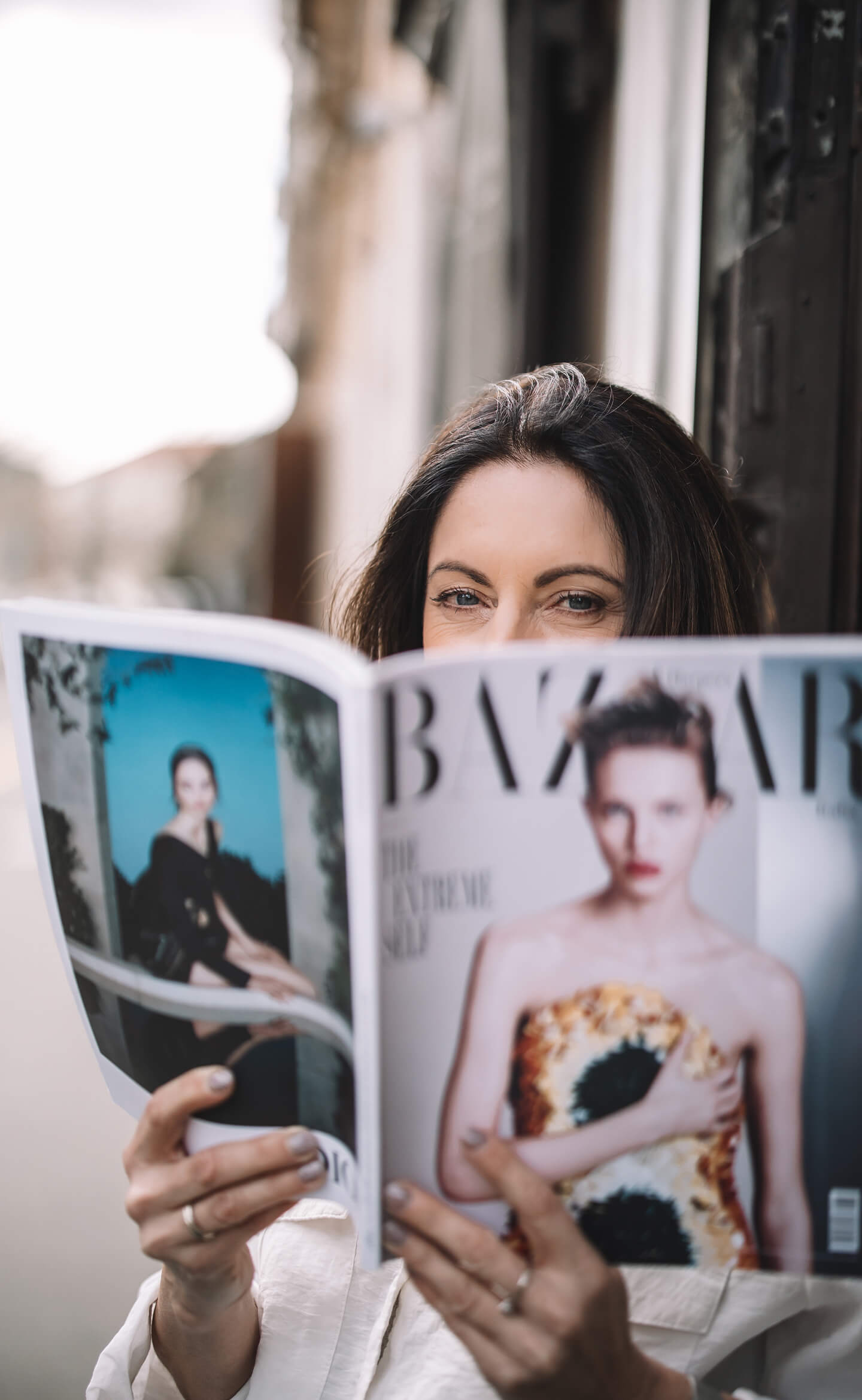 Fiatal nő magazint tart a szeme előtt, játékos portré utcai környezetben