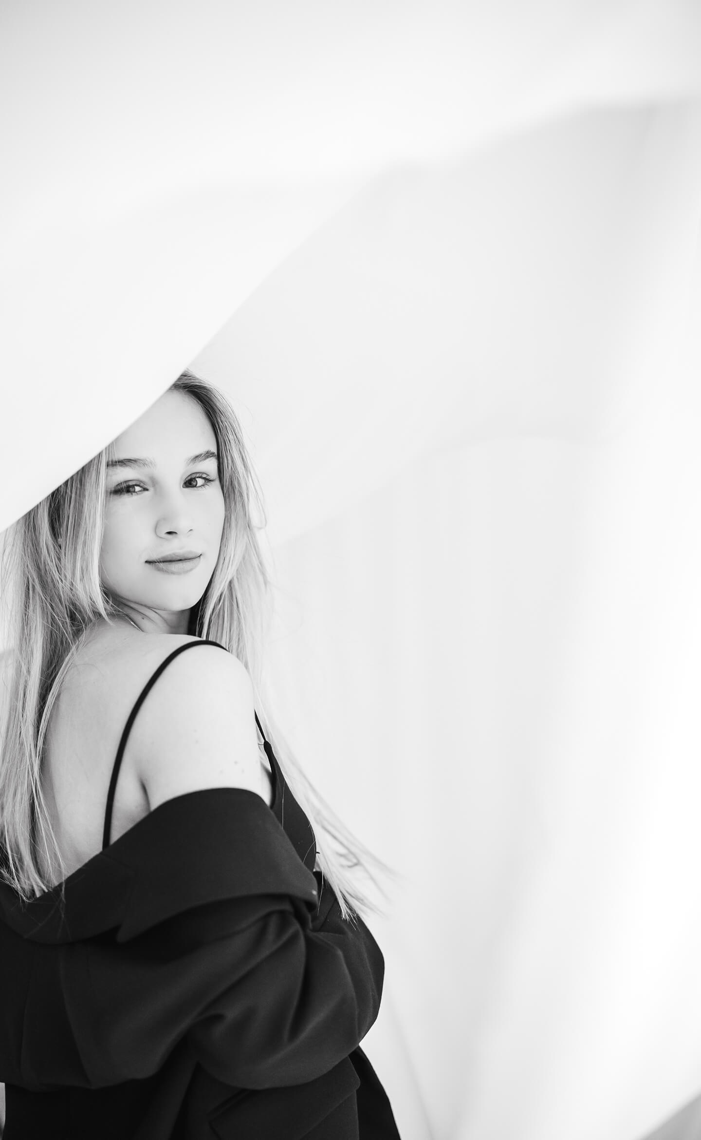 Fiatal nő elegáns fekete ruhában, finom tekintettel, világos háttér előtt